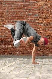 Photo of Man dancing hip hop near brick wall outdoors, low angle view