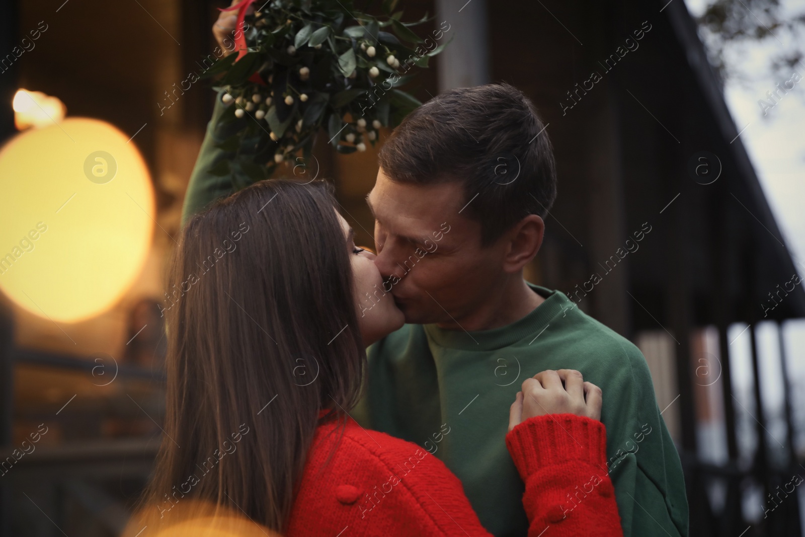 Photo of Happy couple kissing under mistletoe bunch outdoors