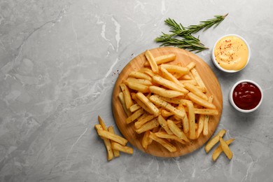 Photo of Delicious french fries served with sauces on grey marble table, flat lay. Space for text