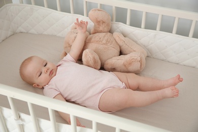 Photo of Cute baby girl with toy in crib at home. Bedtime schedule