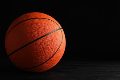 Basketball ball on black wooden table against dark background, space for text