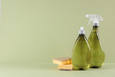 Photo of Bottles of cleaning product and sponges on light green background. Space for text