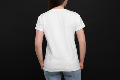 Woman wearing white t-shirt on black background, back view