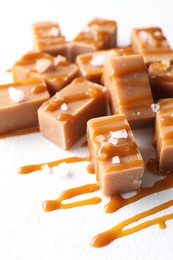 Photo of Tasty candies, caramel sauce and salt on white table, closeup