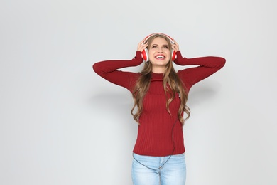 Young woman listening to Christmas music on color background