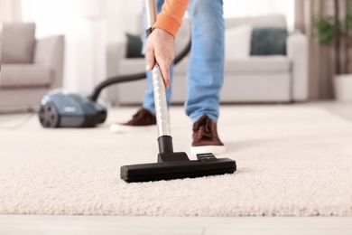 Young man cleaning carpet with vacuum at home