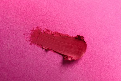 Smear of beautiful lipstick on pink background, top view