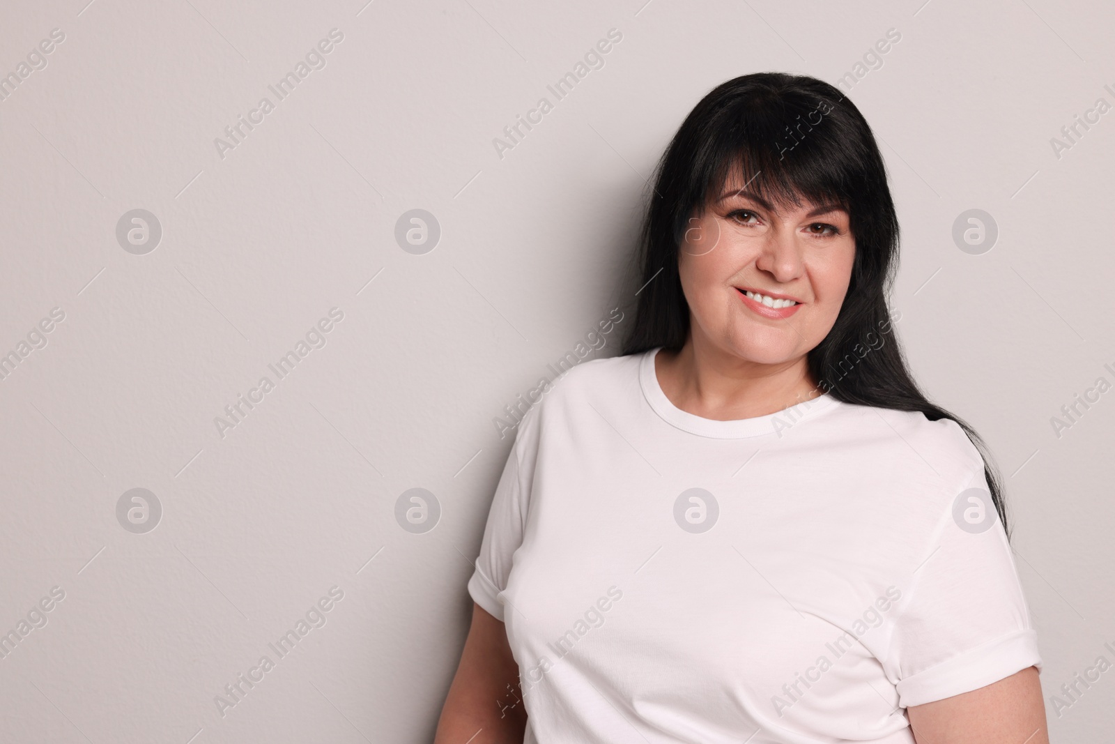 Photo of Beautiful overweight mature woman with charming smile on light grey background. Space for text