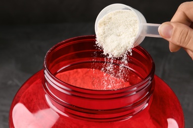 Photo of Woman pouring protein powder from measuring scoop into jar, closeup