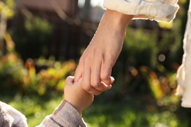 Daughter holding mother's hand outdoors, closeup view