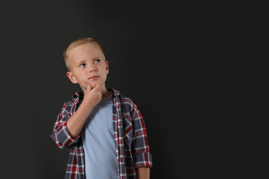 Photo of Pensive little boy on black background, space for text. Thinking about answer to question