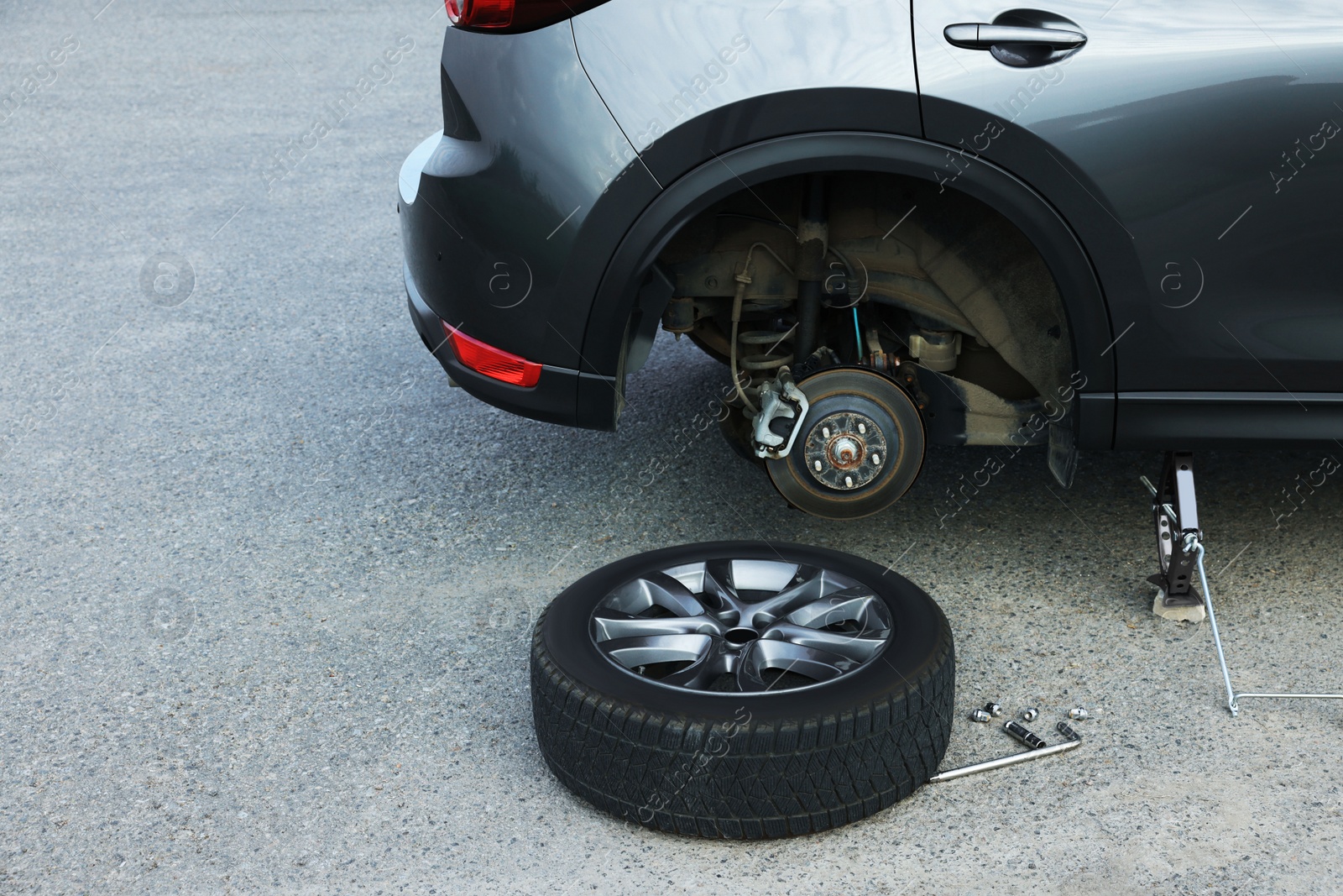 Photo of Car lifted by scissor jack and new wheel on asphalt outdoors. Tire puncture