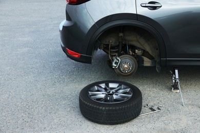 Photo of Car lifted by scissor jack and new wheel on asphalt outdoors. Tire puncture