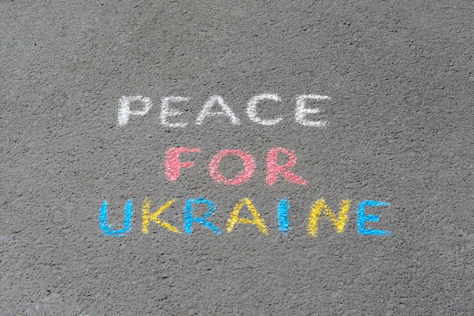 Photo of Words Peace For Ukraine written with colorful chalks on asphalt outdoors