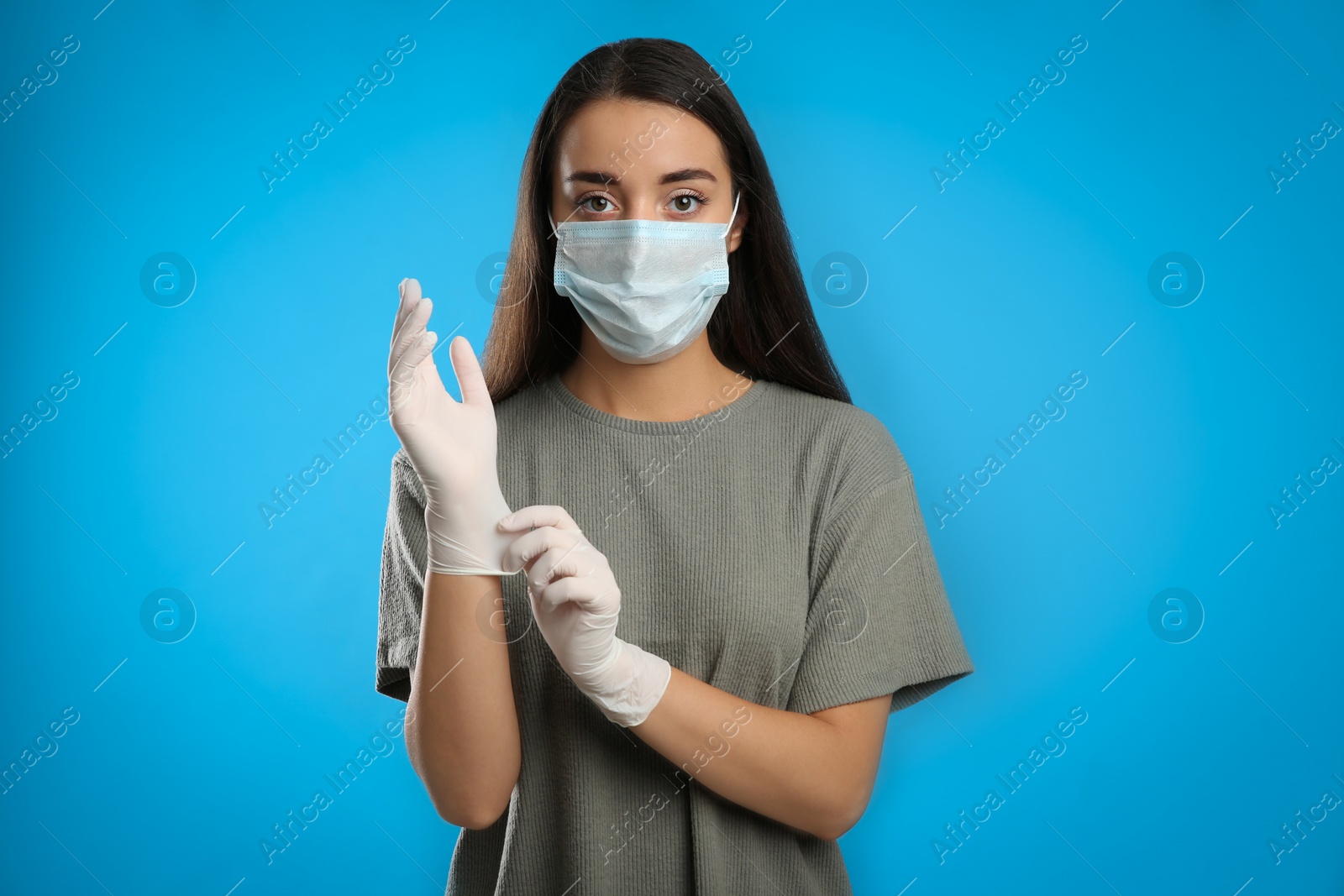 Photo of Woman in protective face mask putting on medical gloves against blue background
