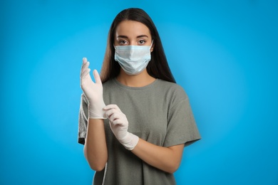 Woman in protective face mask putting on medical gloves against blue background