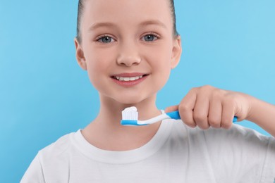 Photo of Happy girl brushing her teeth with toothbrush on light blue background