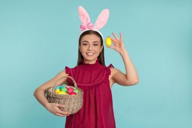 Photo of Beautiful woman in bunny ears headband with Easter eggs on color background