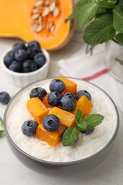 Photo of Bowl of delicious rice porridge with blueberries, pumpkin and mint on table, closeup