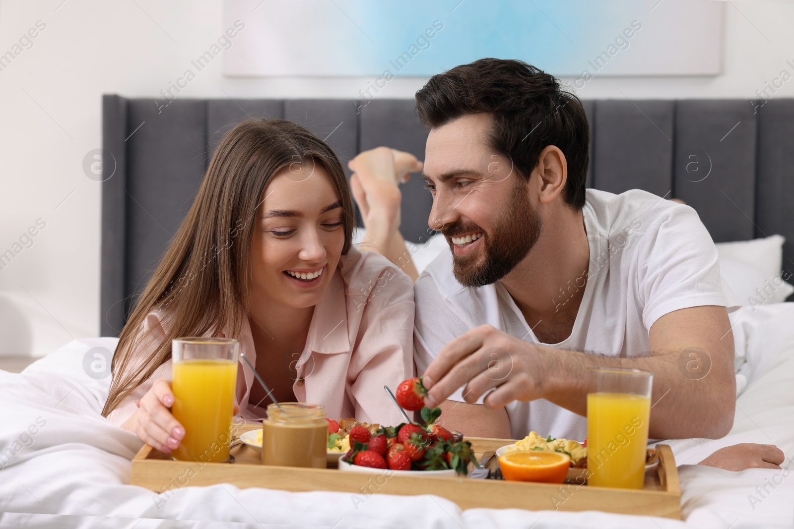 Photo of Happy couple eating tasty breakfast on bed at home