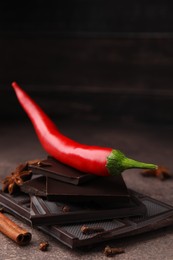 Photo of Delicious chocolate, fresh red chili pepper and spices on grey textured table, closeup
