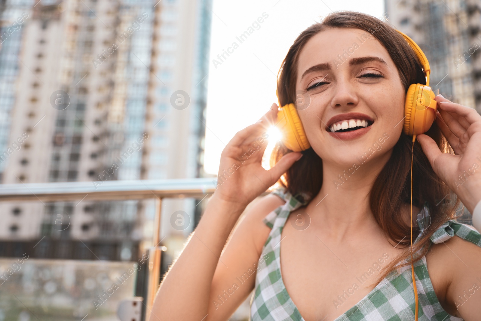 Photo of Beautiful young woman listening to music with headphones on sunny day outdoors, space for text