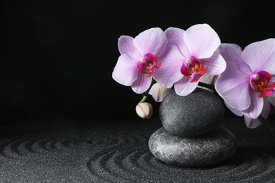 Spa stones and orchid flowers on black sand with beautiful pattern, space for text. Zen concept