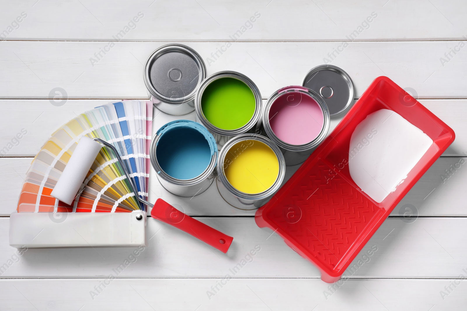 Photo of Cans of paints, roller, tray and palette on white wooden background, flat lay