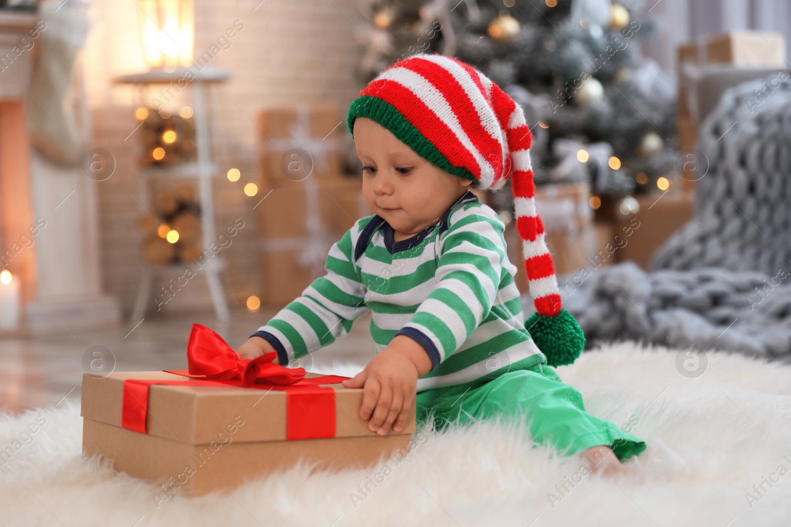 Photo of Little baby with elf hat and Christmas gift on floor at home