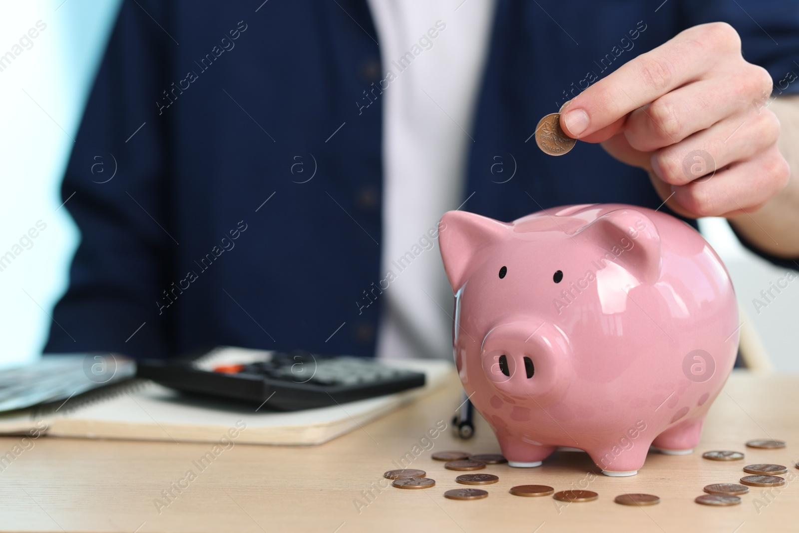 Photo of Financial savings. Man putting coin into piggy bank at wooden table, closeup