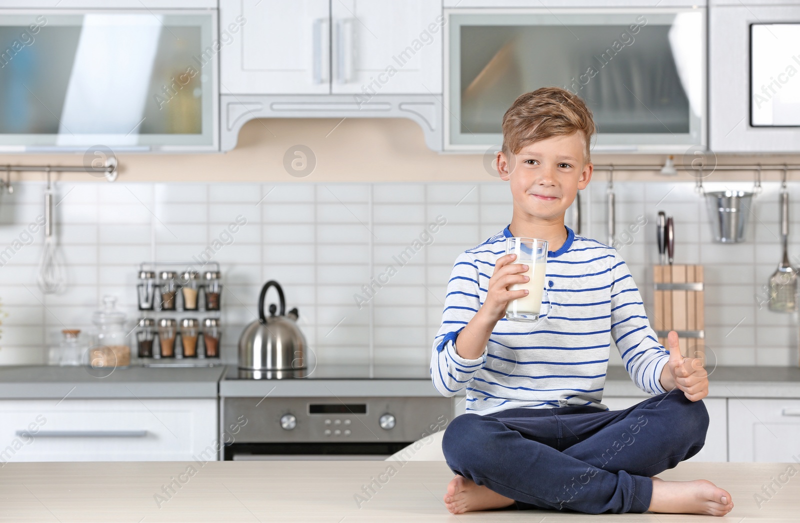 Photo of Adorable little boy with glass of milk in kitchen