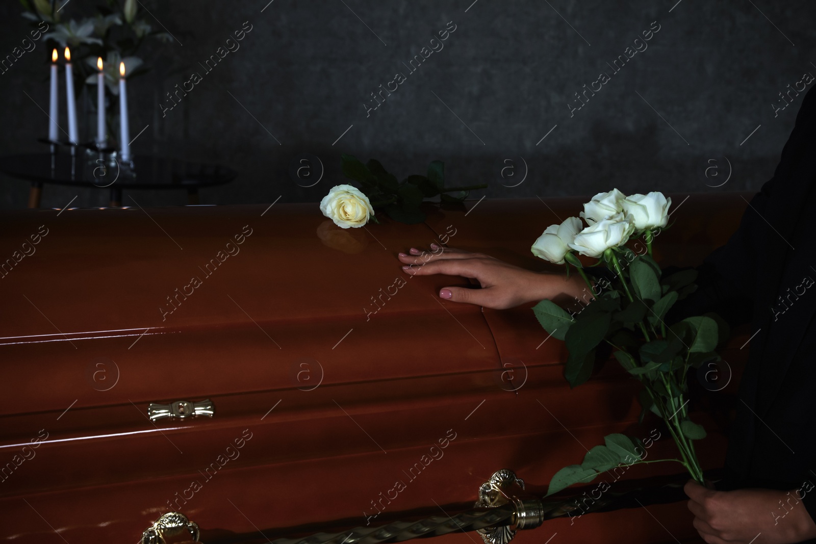 Photo of Young woman with white roses near casket in funeral home, closeup