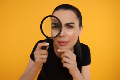 Photo of Woman looking through magnifier glass on yellow background