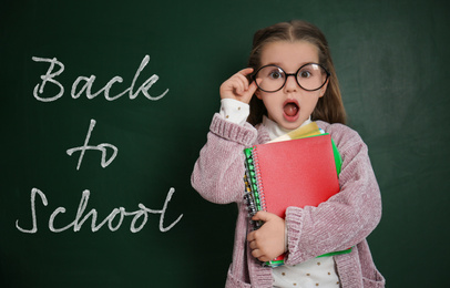 Image of Cute little child wearing glasses near chalkboard with phrase BACK TO SCHOOL