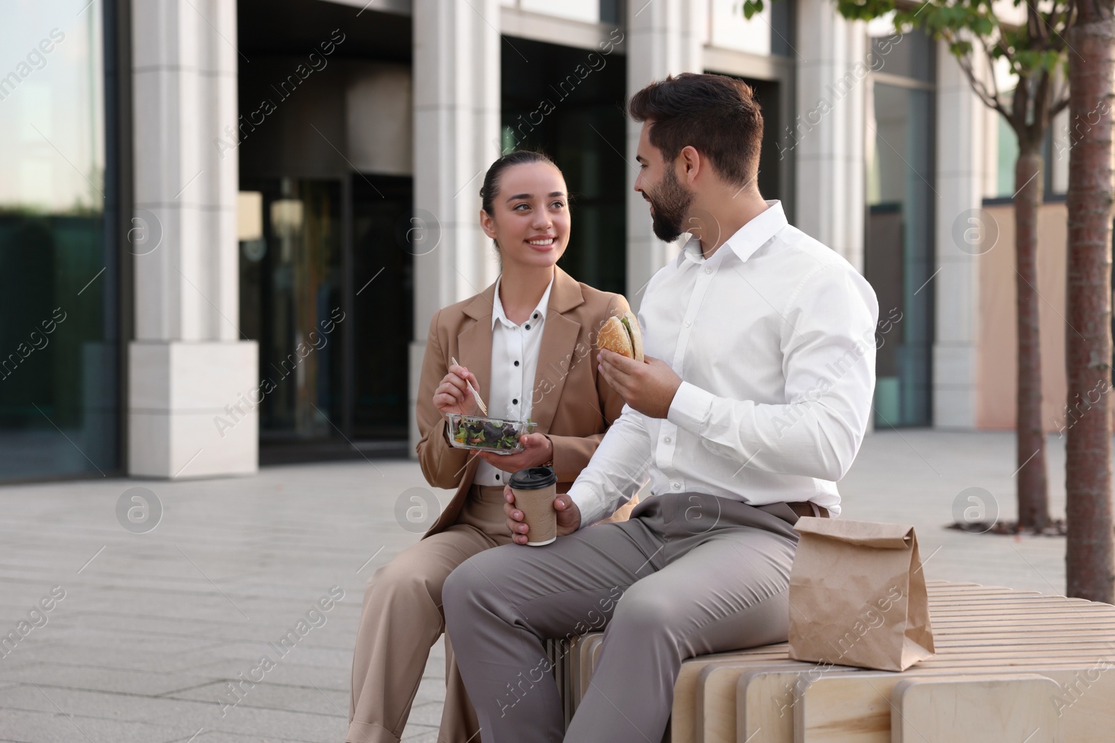 Photo of Happy colleagues having business lunch together on bench outdoors