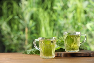 Photo of Aromatic nettle tea and green leaves on wooden table outdoors, space for text