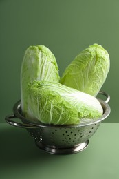 Fresh Chinese cabbages in colander on green background