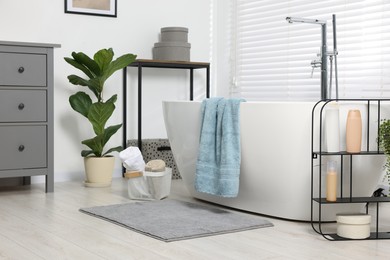 Photo of Stylish bathroom interior with bath tub, houseplant and soft light grey mat