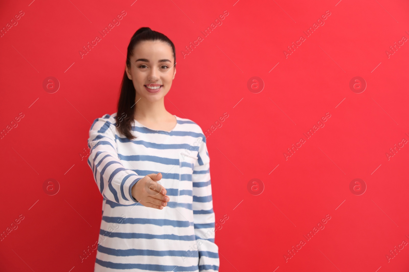 Photo of Happy young woman offering handshake against red background, focus on hand. Space for text