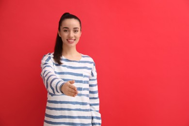 Photo of Happy young woman offering handshake against red background, focus on hand. Space for text