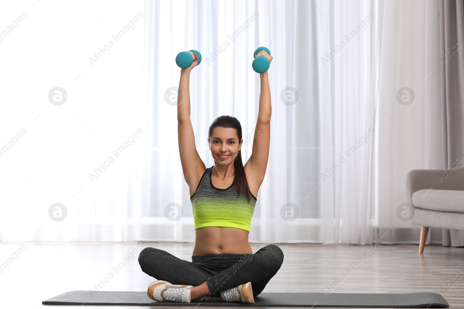 Photo of Young woman in fitness clothes doing exercise with dumbbells at home