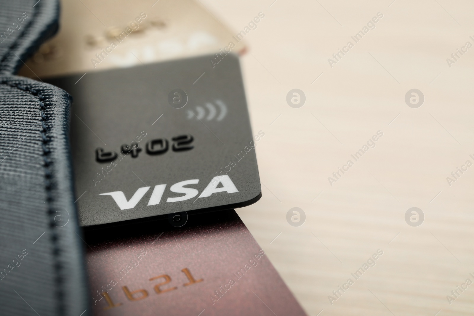 Photo of MYKOLAIV, UKRAINE - FEBRUARY 23, 2022: Bank cards of Visa payment system in leather wallet on wooden table, closeup. Space for text