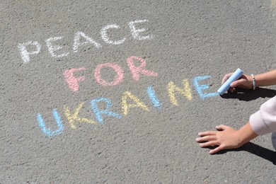 Girl writing Peace For Ukraine with colorful chalks on asphalt outdoors, closeup