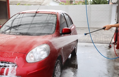 Man cleaning auto with high pressure water jet at car wash