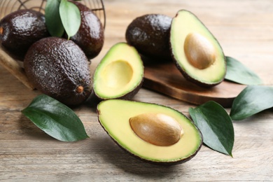 Photo of Whole and cut avocados with green leaves on wooden table