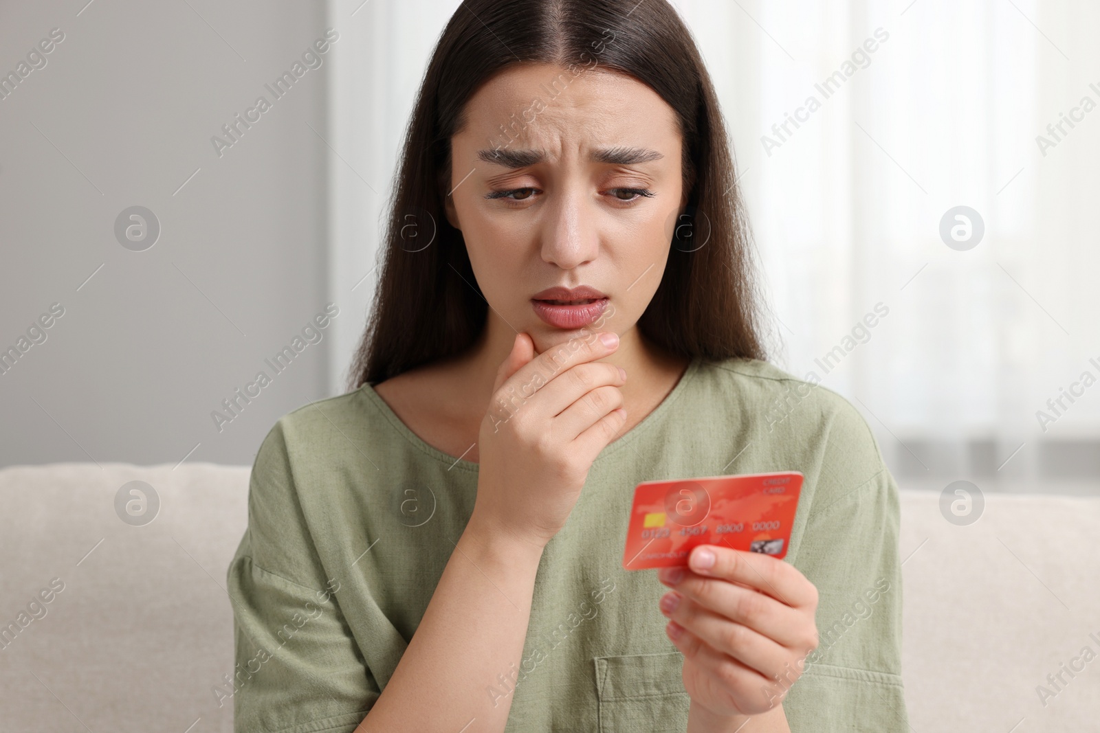 Photo of Confused woman with credit card at home. Be careful - fraud