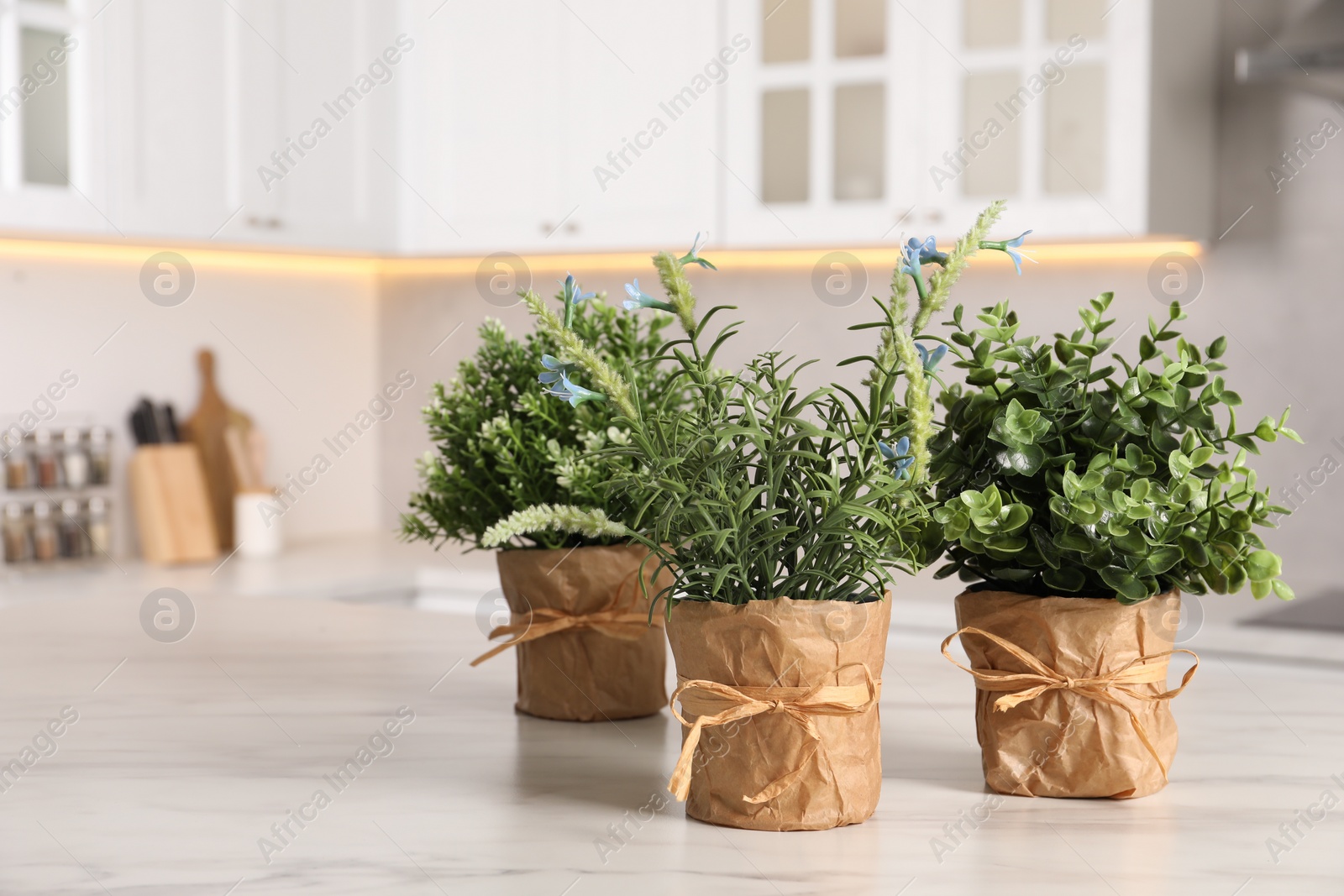 Photo of Artificial potted herbs on white marble table in kitchen, space for text. Home decor