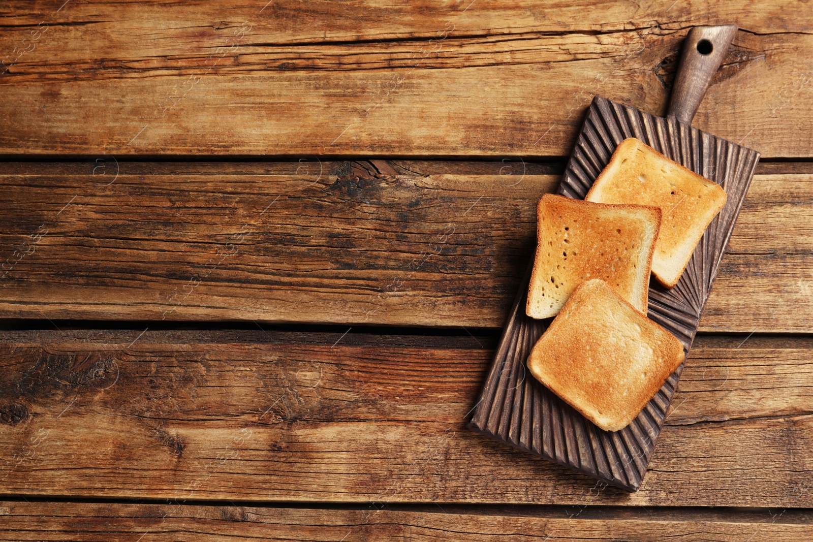 Photo of Slices of tasty toasted bread on wooden table, top view. Space for text