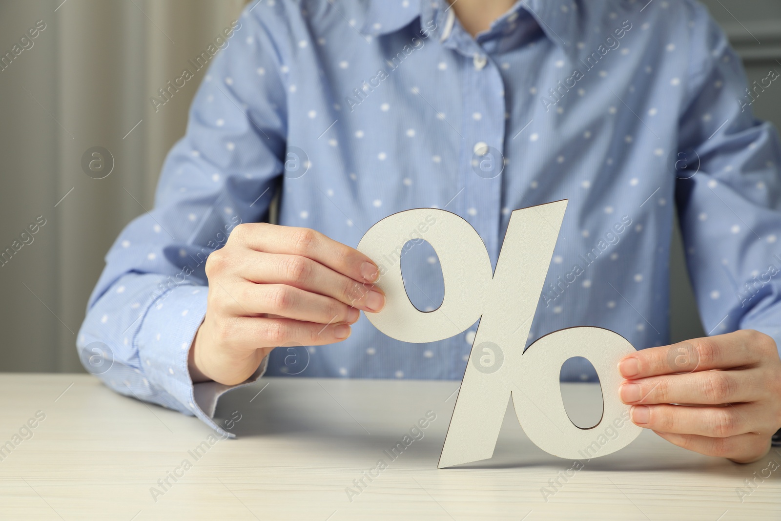 Photo of Woman holding percent sign at white wooden table, closeup