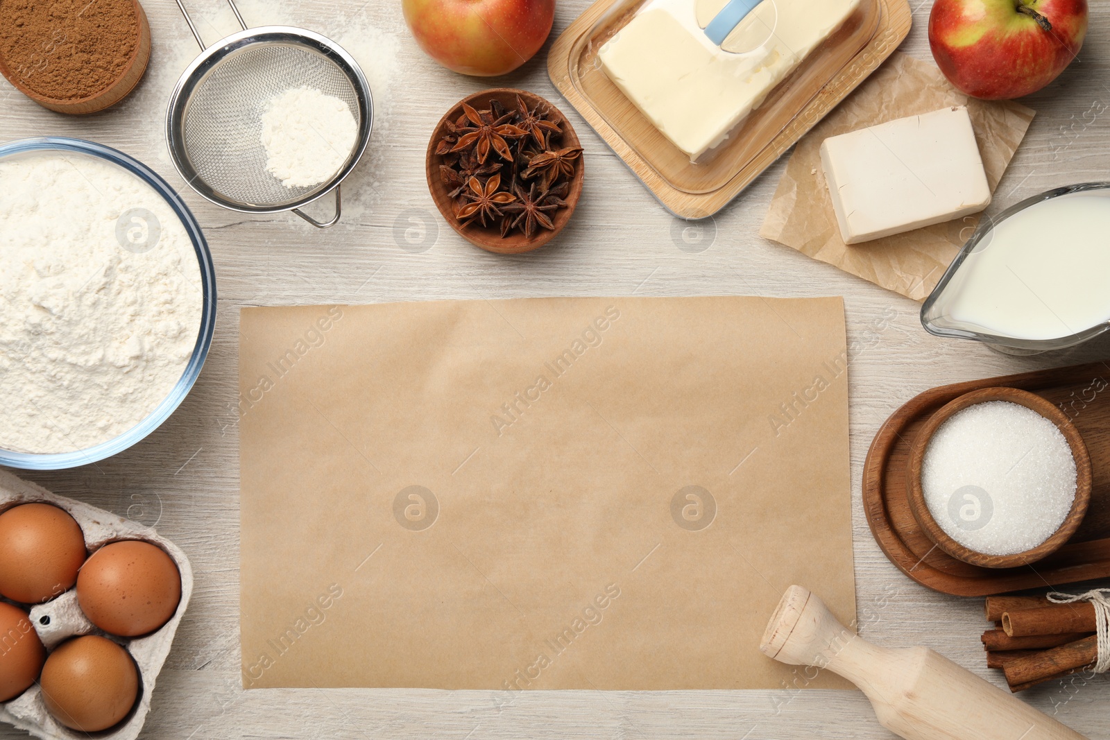 Photo of Flat lay composition with piece of empty parchment paper and different ingredients on wooden table. Cooking yeast cake